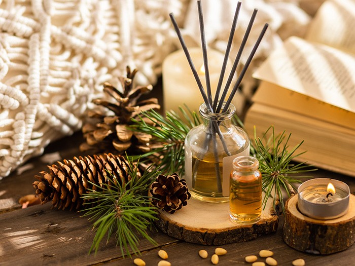 End table featuring pinecones and pine branches alongside wooden coasters topped with candles and essential oils.